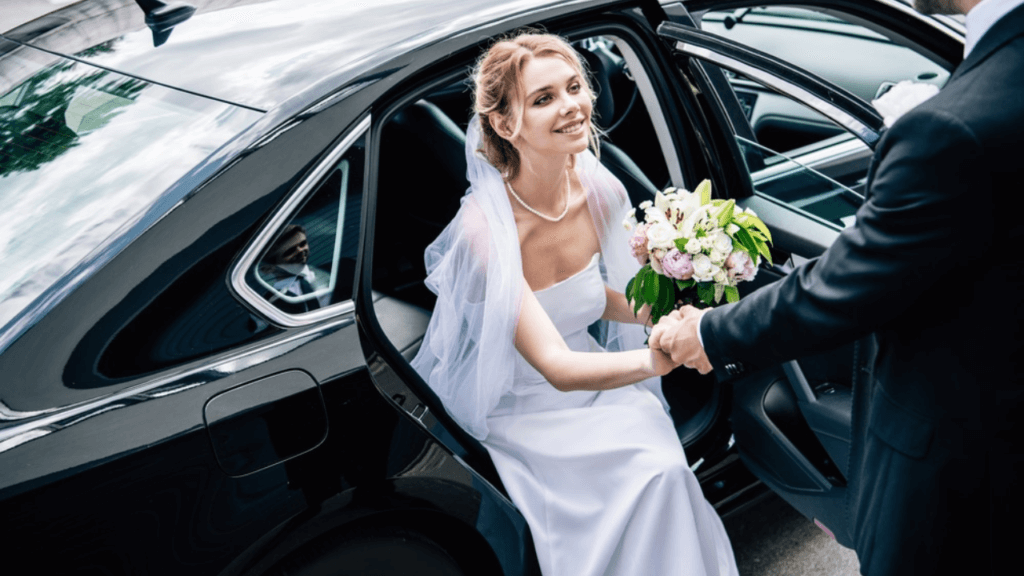 Bride stepping out of a luxury wedding car in front of a cathedral, with a professional chauffeur in formal suit holding the door open—elegant wedding transport service in London.